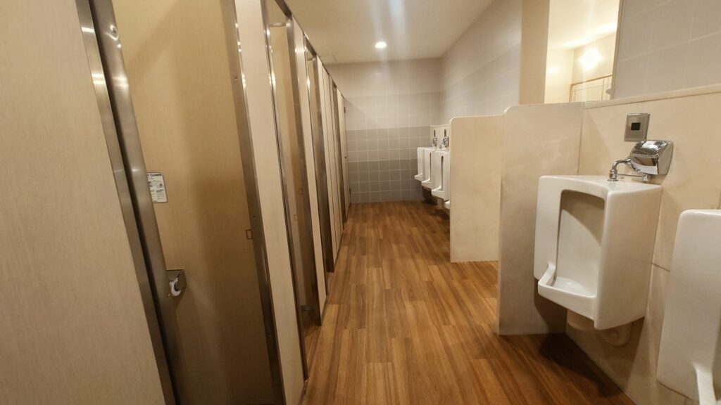 ウッド調の床に個室と小便器が並ぶ、明るく清潔な男性用トイレ